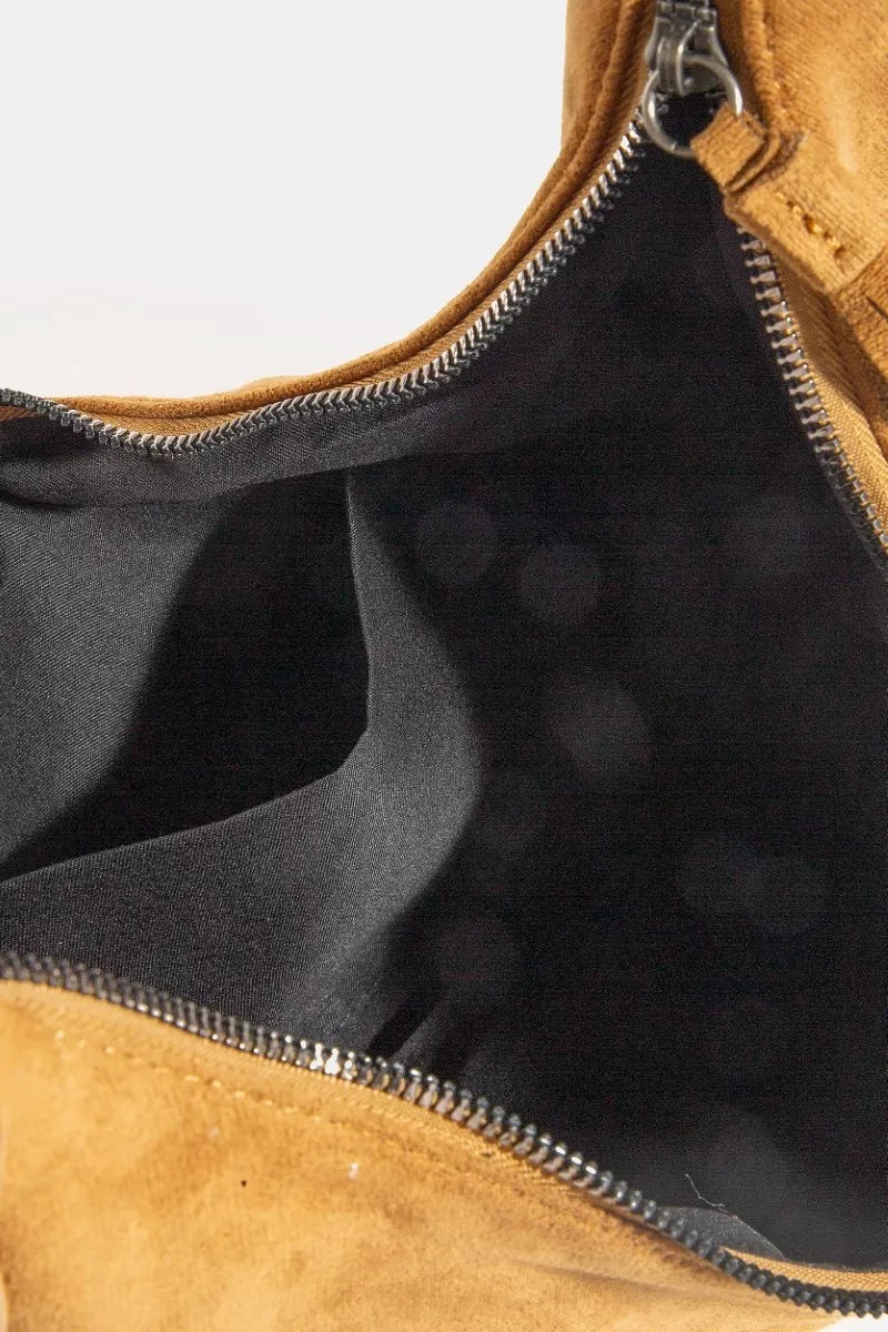 Close-up of a brown leather bag with a zipper, showing black interior lining.