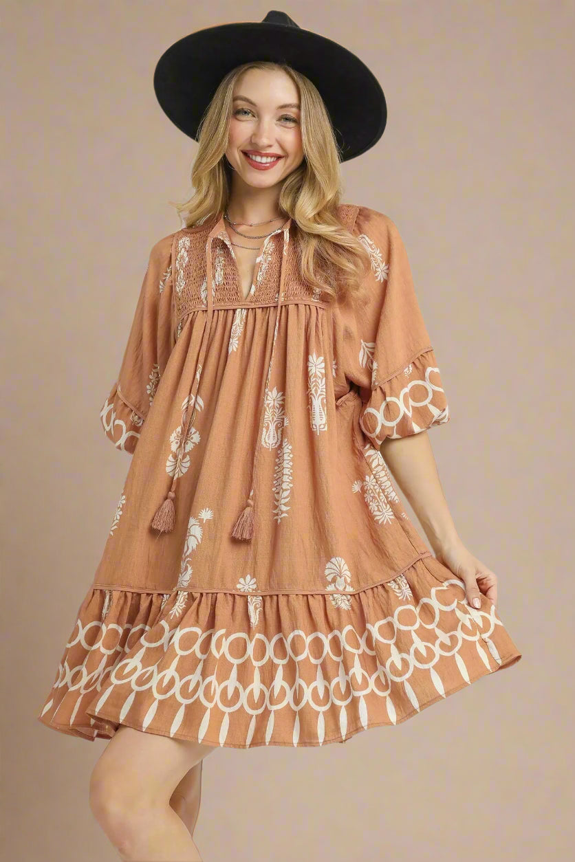 Woman wearing a brown dress with white patterns and a black hat on a white background
