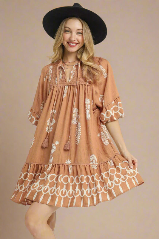 Woman wearing a brown dress with white patterns and a black hat on a white background