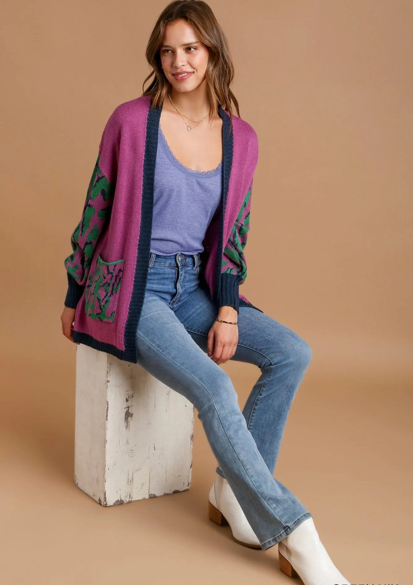 Woman wearing a colorful cardigan, blue jeans, and white boots on a beige background