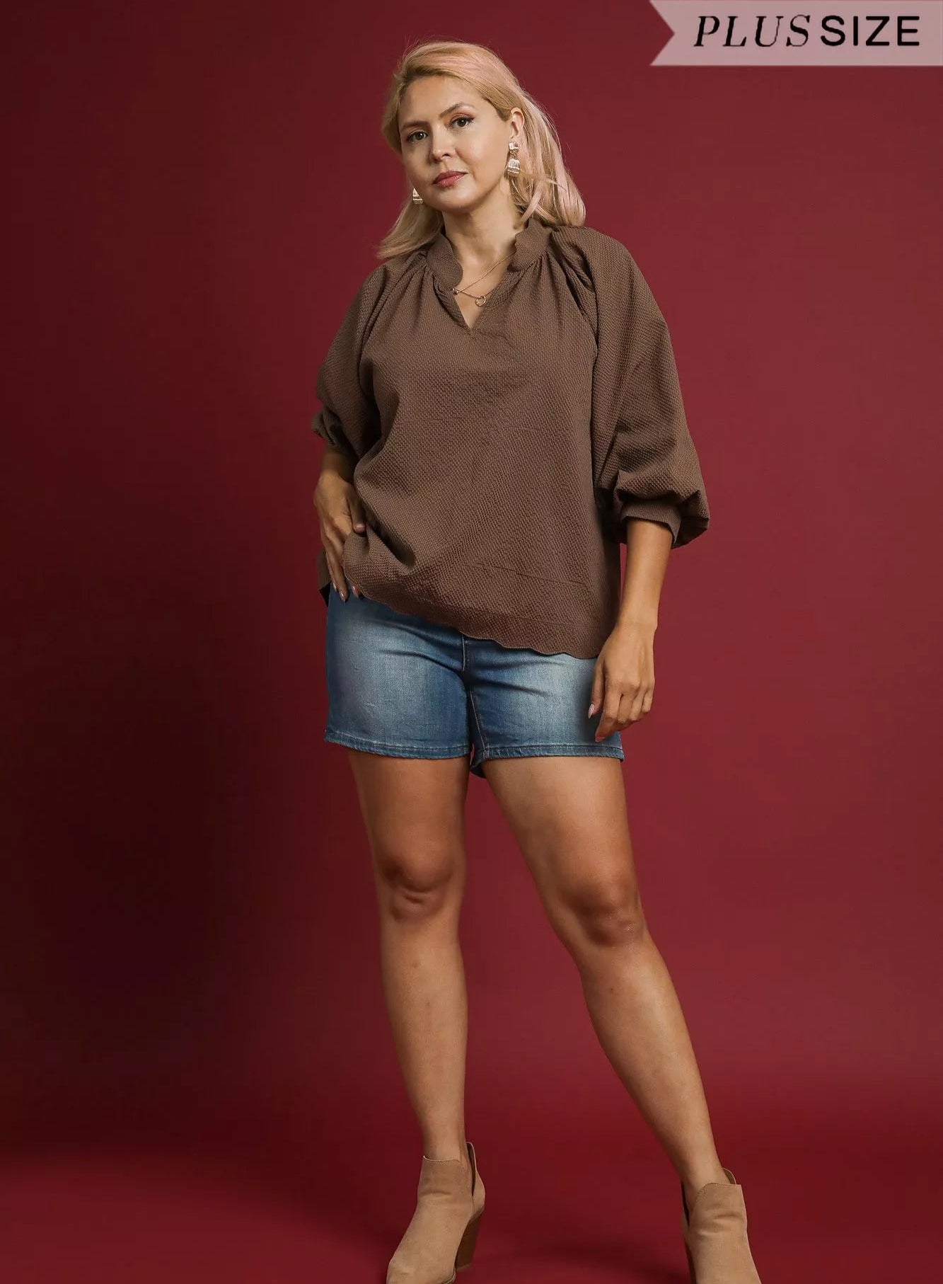 Woman wearing a brown blouse and denim shorts on a red background
