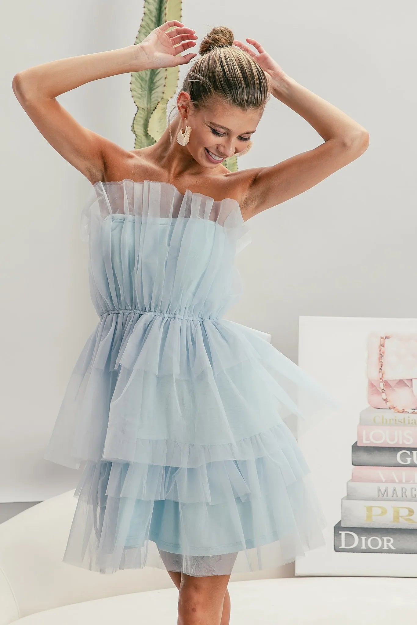 Woman wearing a light blue strapless dress with a white background and books in the background.