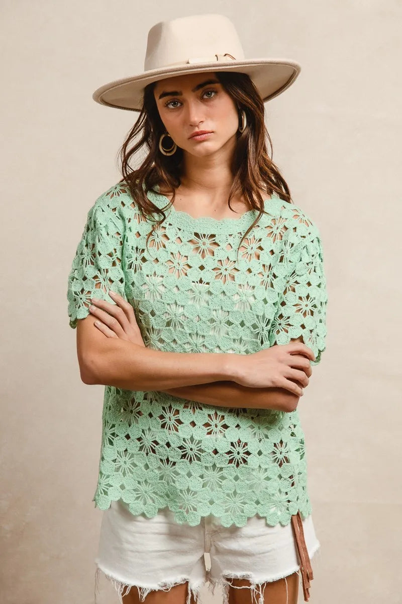 Woman wearing a light green lace top and beige hat against a beige background