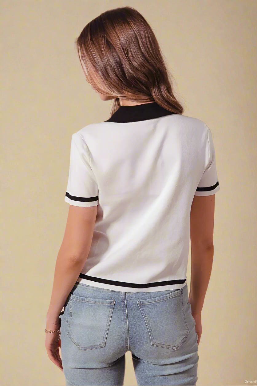 Person wearing a white polo shirt with black trim and blue jeans on a beige background