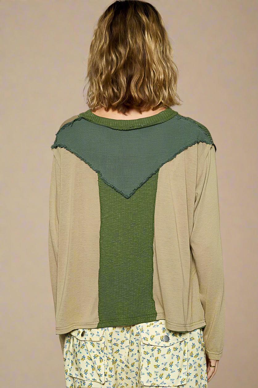 Person wearing a green and beige long-sleeve top with a geometric pattern on a plain background