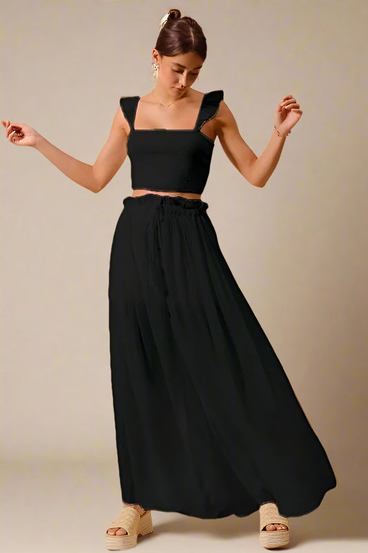 Woman wearing a black top and long black skirt against a beige background