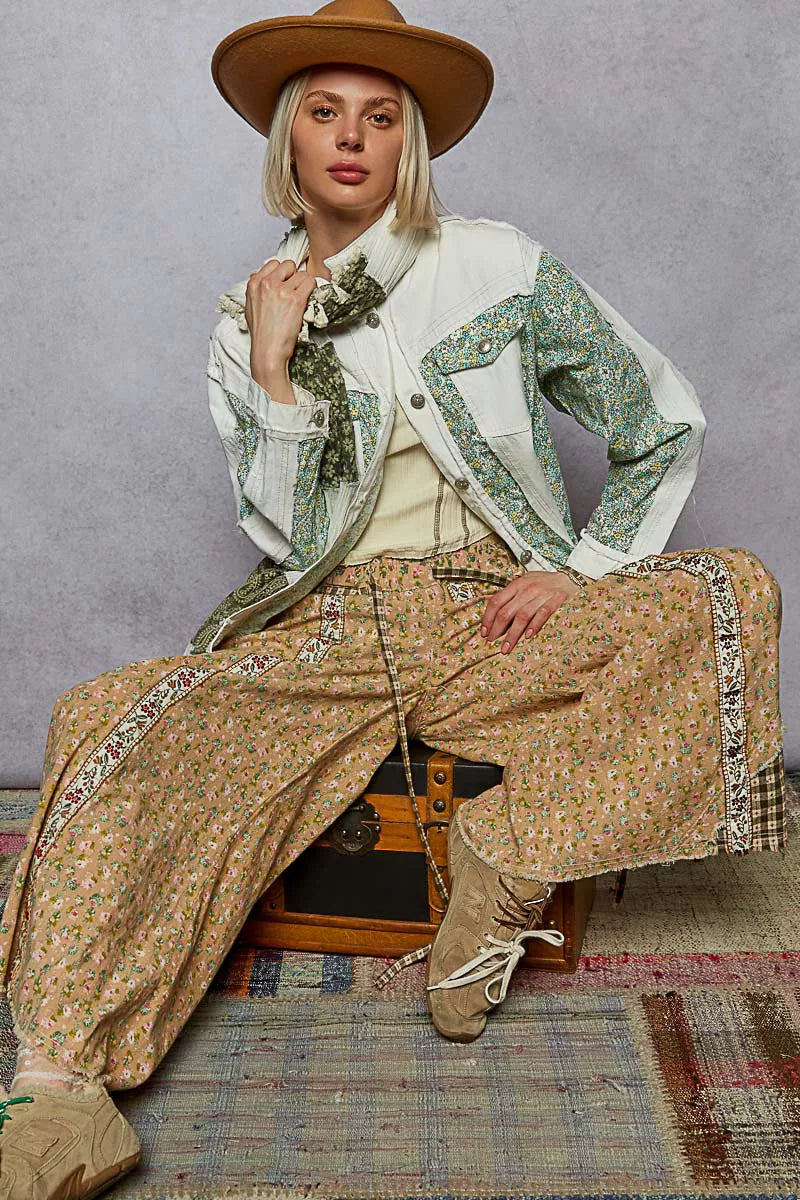 Person wearing a stylish outfit with a hat, jacket, and pants on a textured floor.