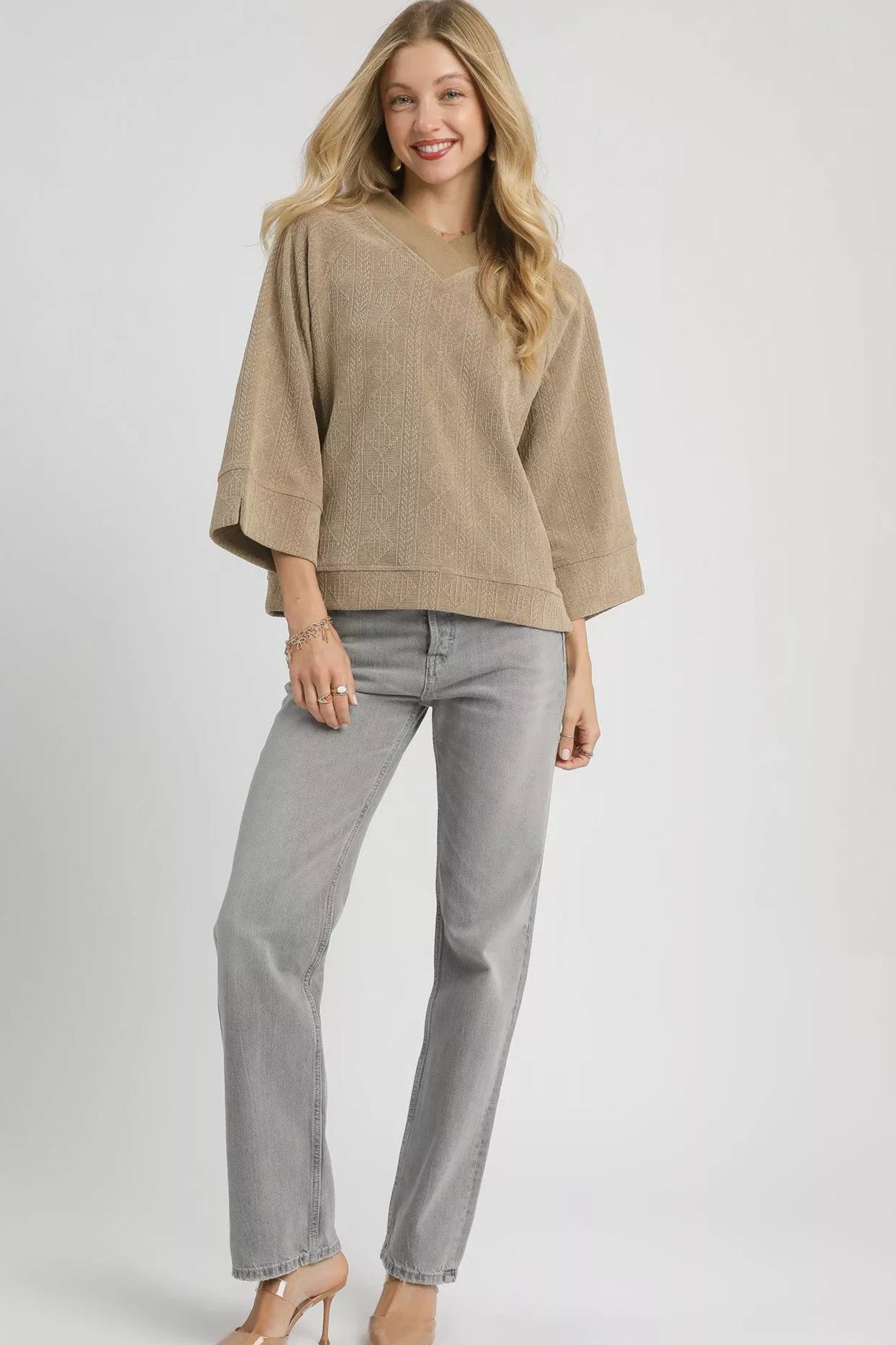 Woman wearing a beige sweater and gray pants on a white background