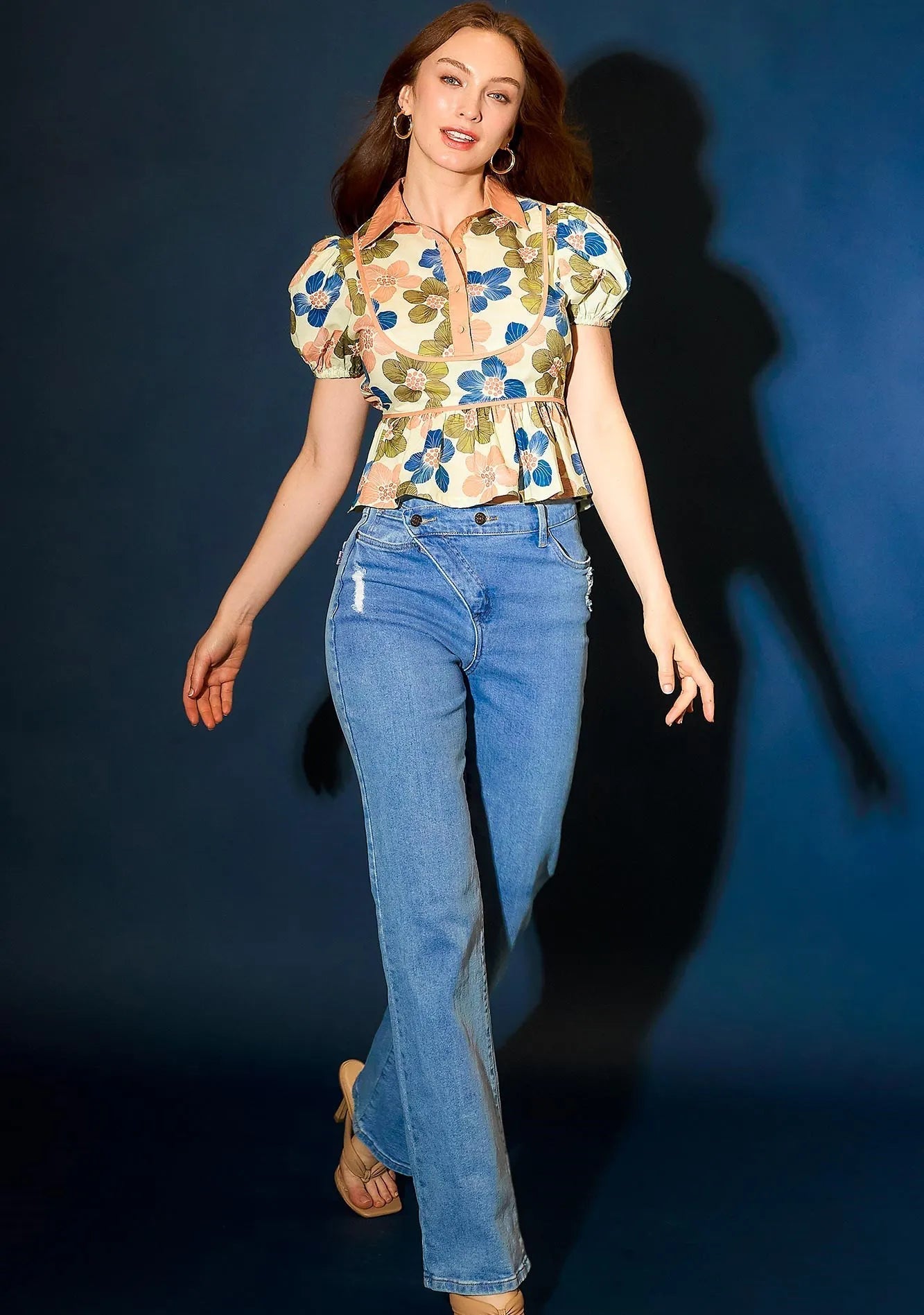 Woman wearing a floral top and blue jeans against a dark background
