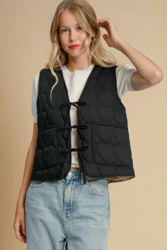 Woman wearing a black puffer vest over a white shirt and blue jeans on a light beige background.
