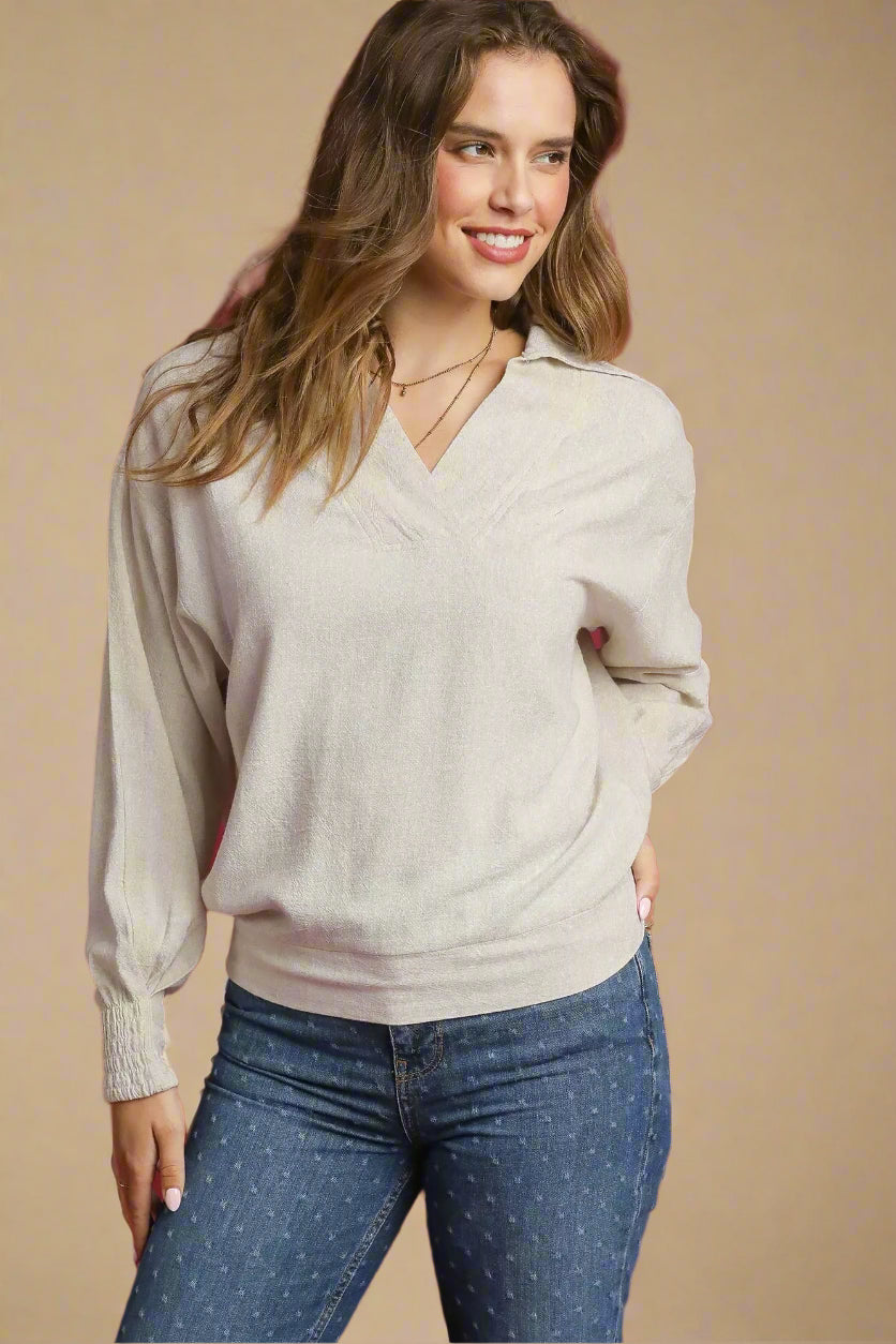Woman wearing a beige sweater and blue jeans against a red background