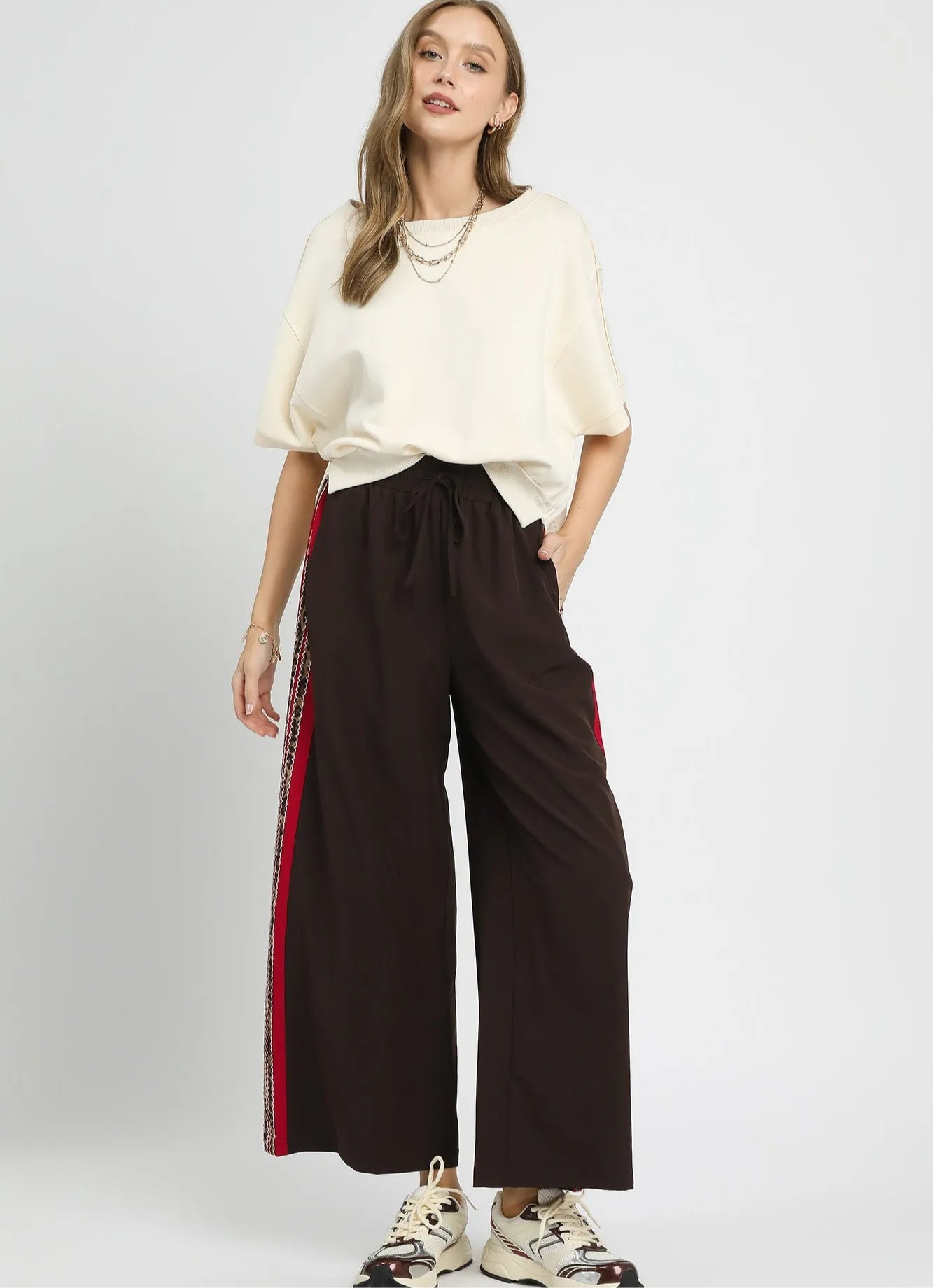 Woman wearing a white top and brown wide-leg pants with red stripes on a white background