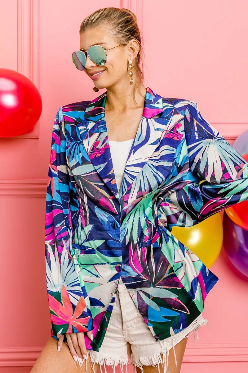 Woman wearing a colorful tropical leaf patterned jacket against a pink background with balloons.