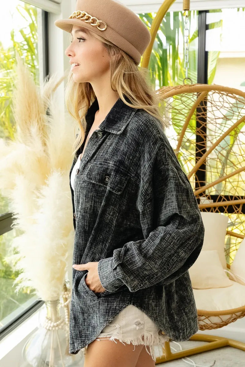 Woman wearing a gray oversized shirt and beige hat in a bright room with plants and a chair.