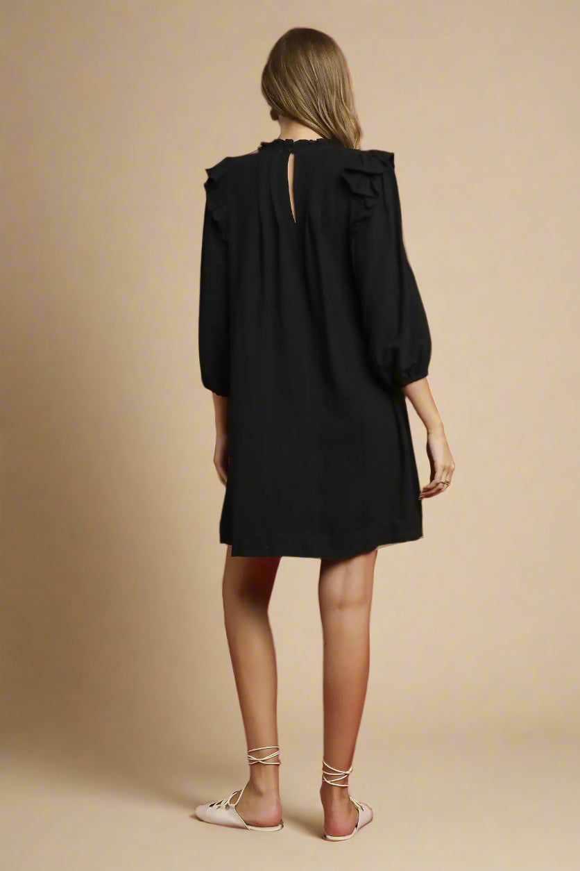 Person wearing a black dress with ruffled shoulders on a beige background