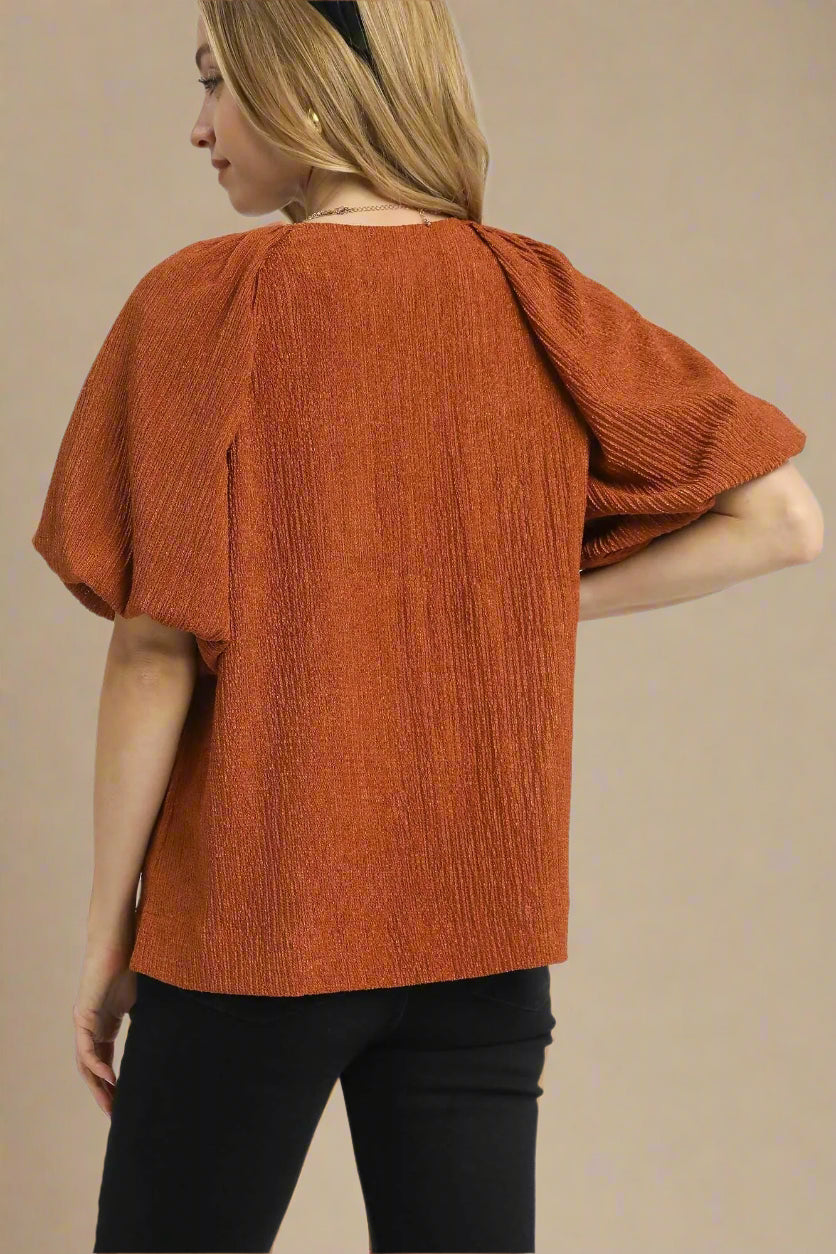 Person wearing a rust-colored textured top on a white background