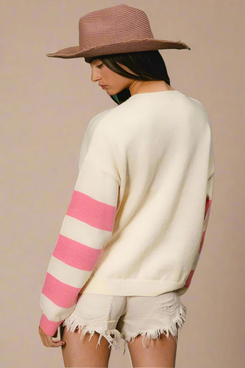 Person wearing a cream sweater with pink stripes and a brown hat against a green background