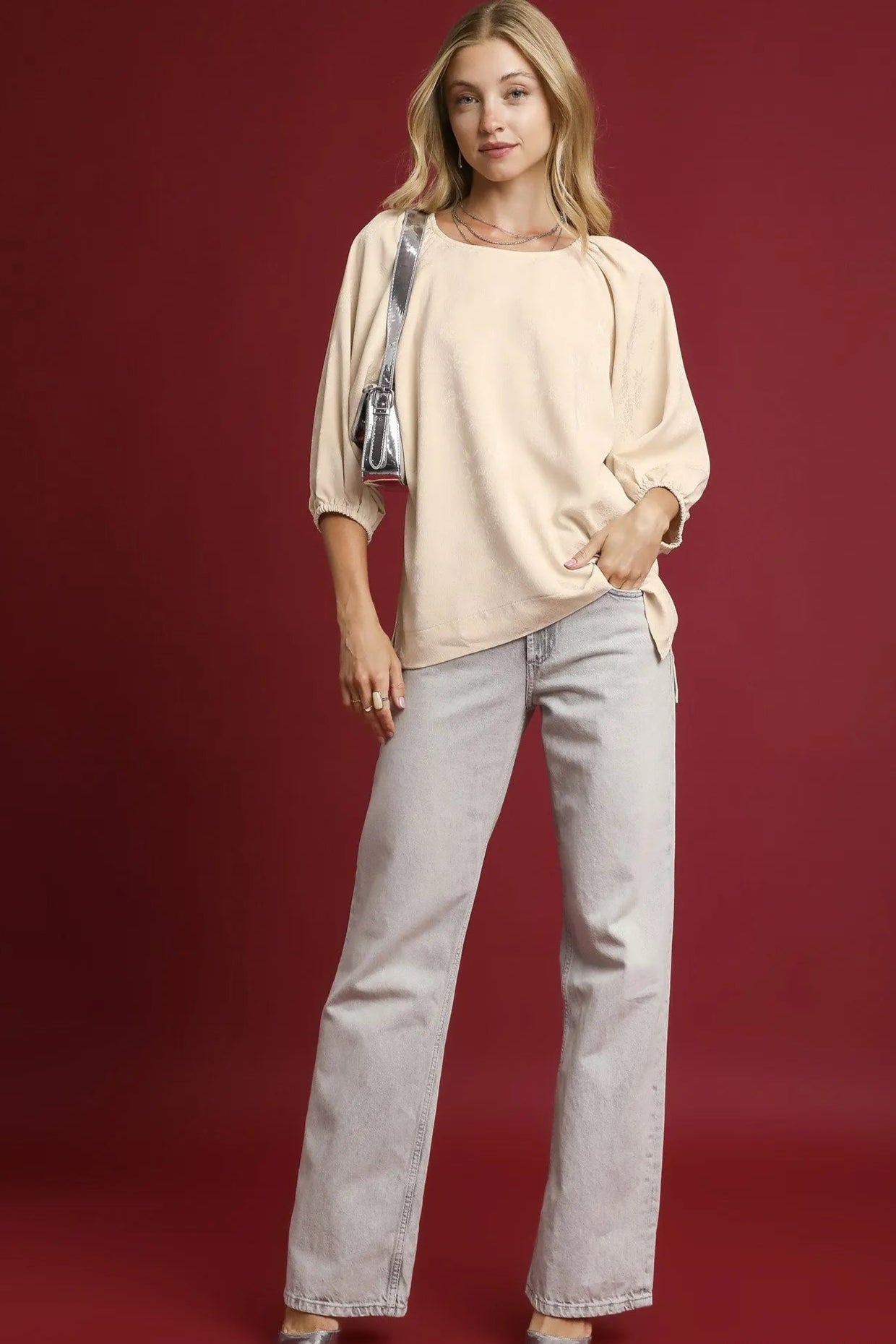 Woman wearing a beige top and light gray jeans against a red background