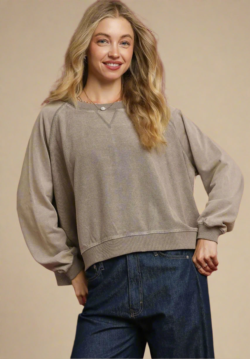 Woman wearing a beige sweater and blue jeans against a red background