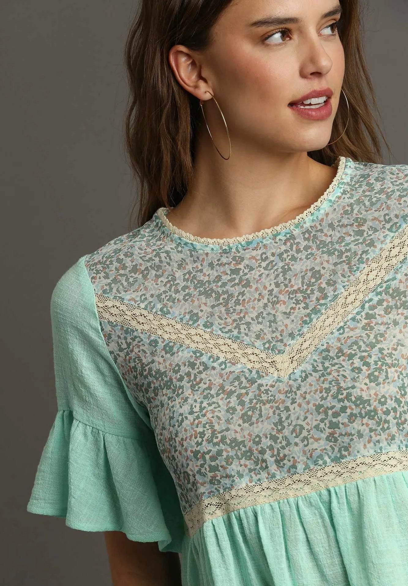Woman wearing a mint green blouse with floral lace details on a gray background