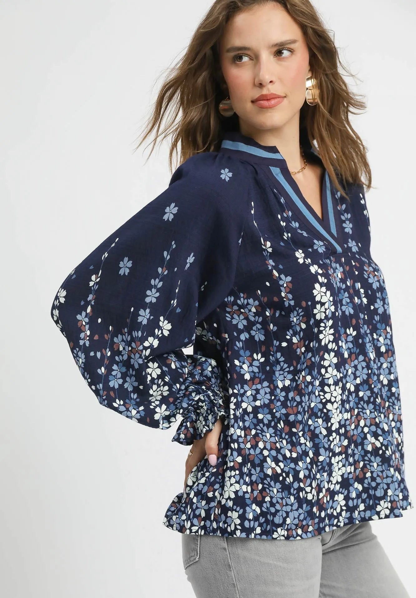 Woman wearing a navy floral blouse with gray pants on a white background