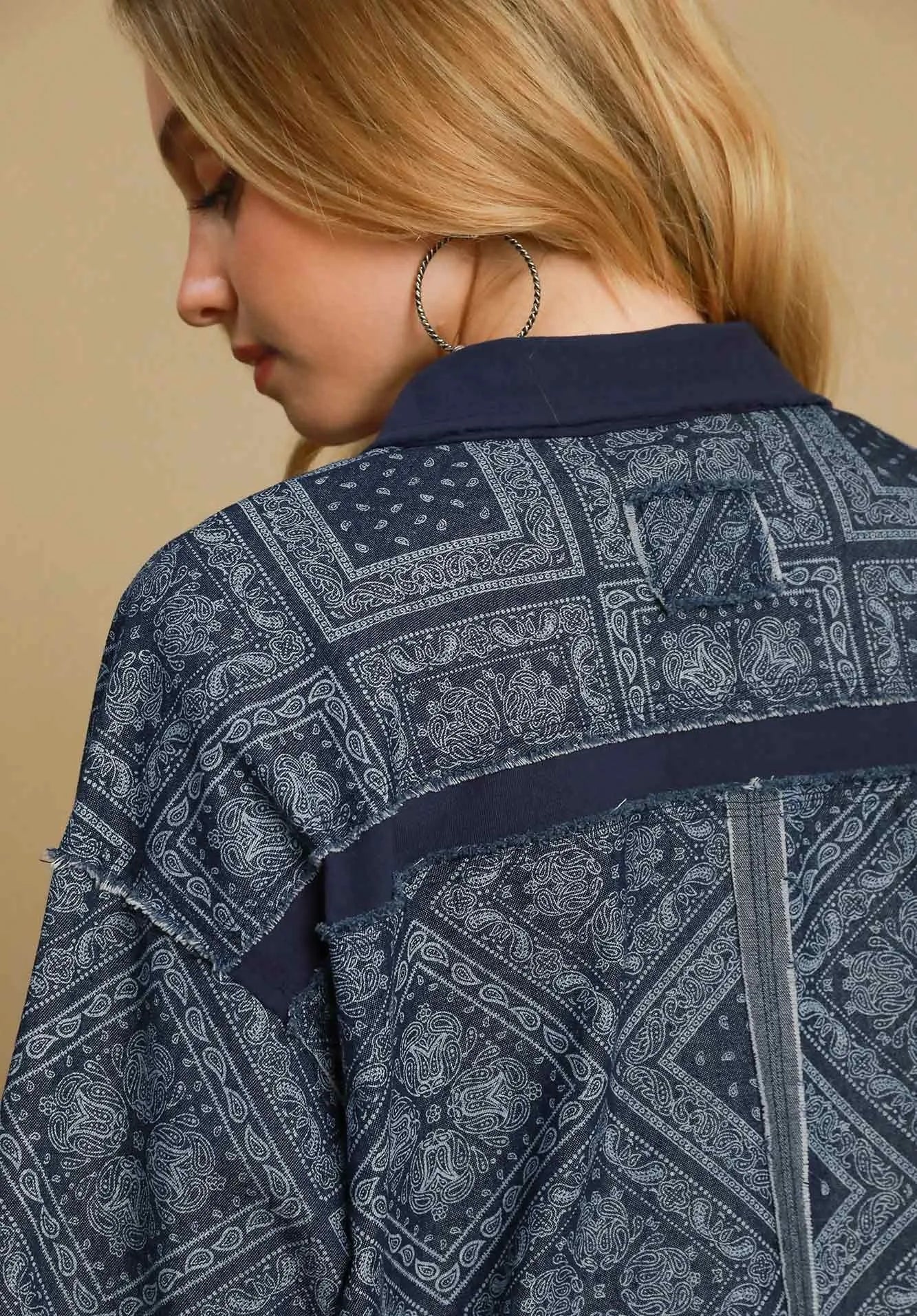 Person wearing a dark denim shirt with a pattern, on a beige background