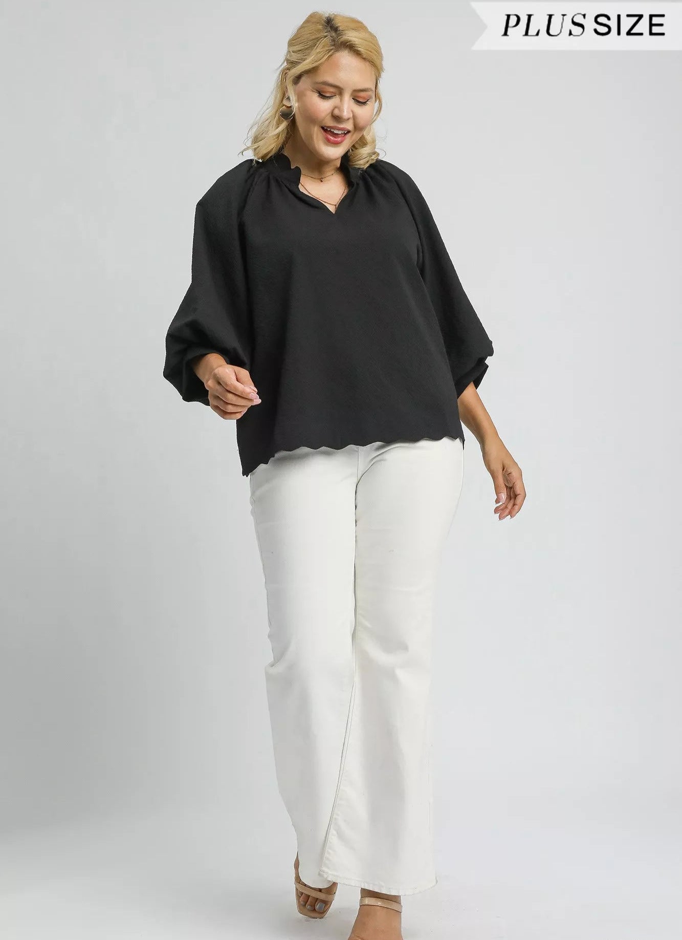 Woman wearing a black blouse and white pants on a gray background