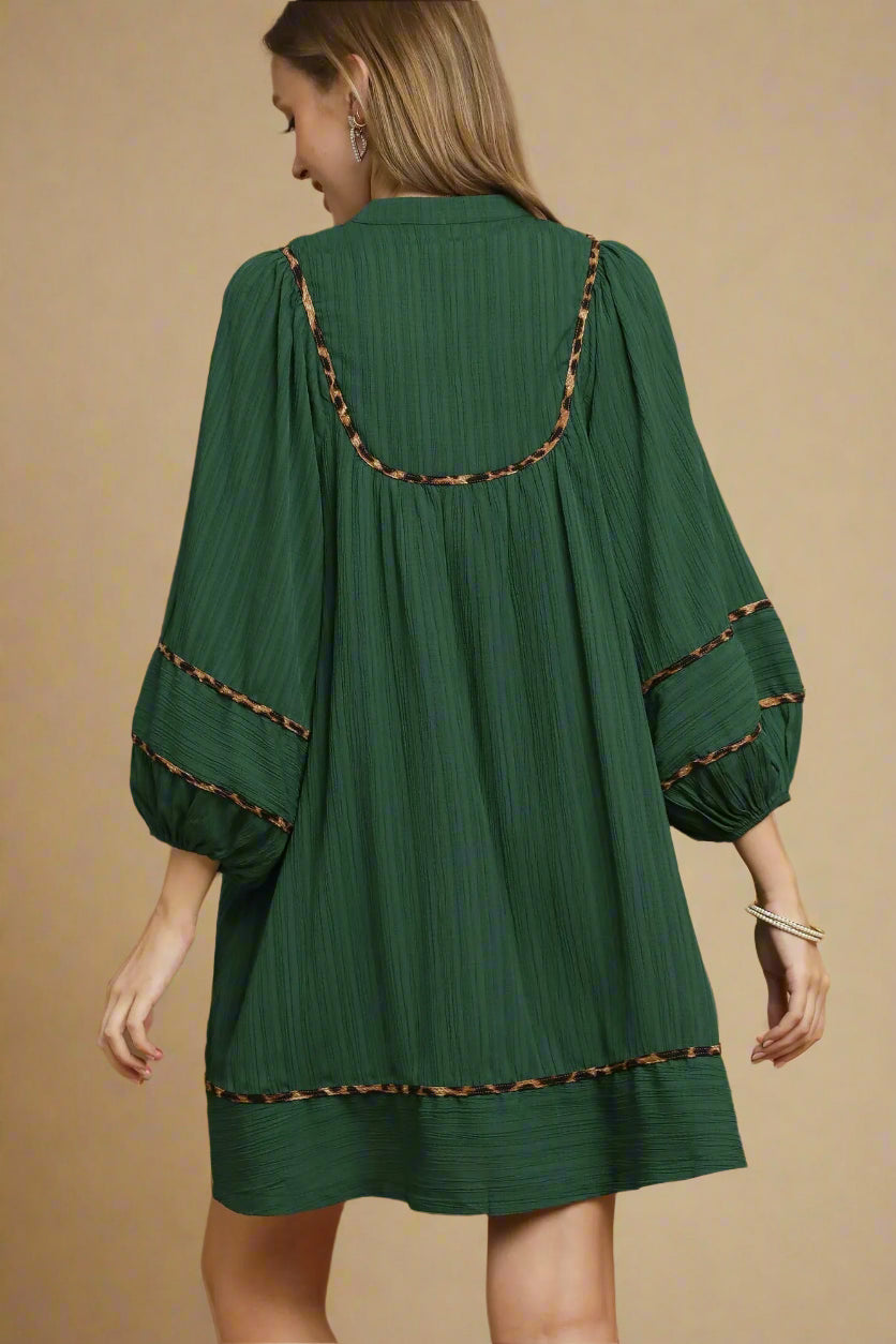 Woman wearing a green dress with brown trim on a beige background