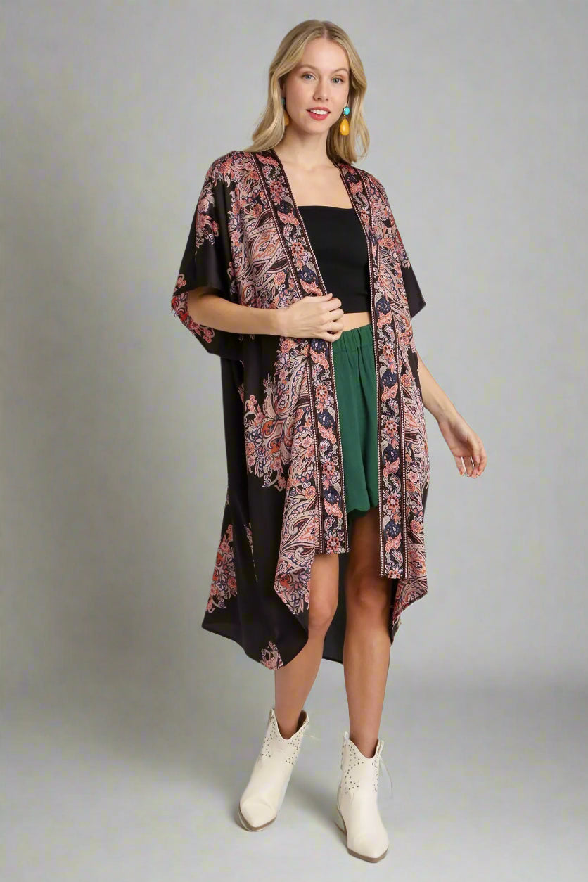 Woman wearing a floral kimono over a black top and green skirt on a white background