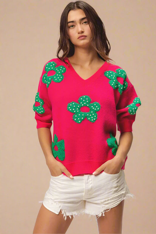 Woman wearing a pink sweater with green floral patterns on a plain background