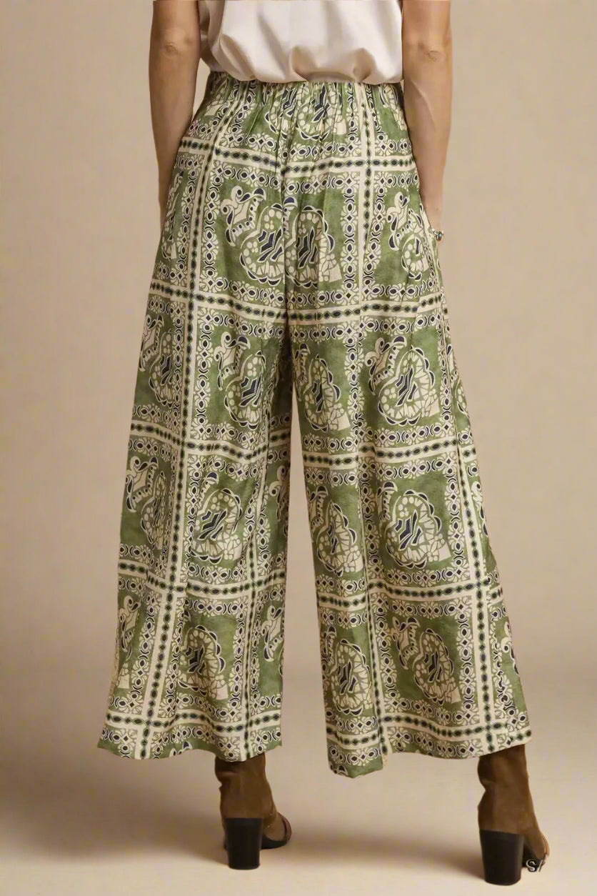 Green patterned wide-leg pants worn by a person on a brown background
