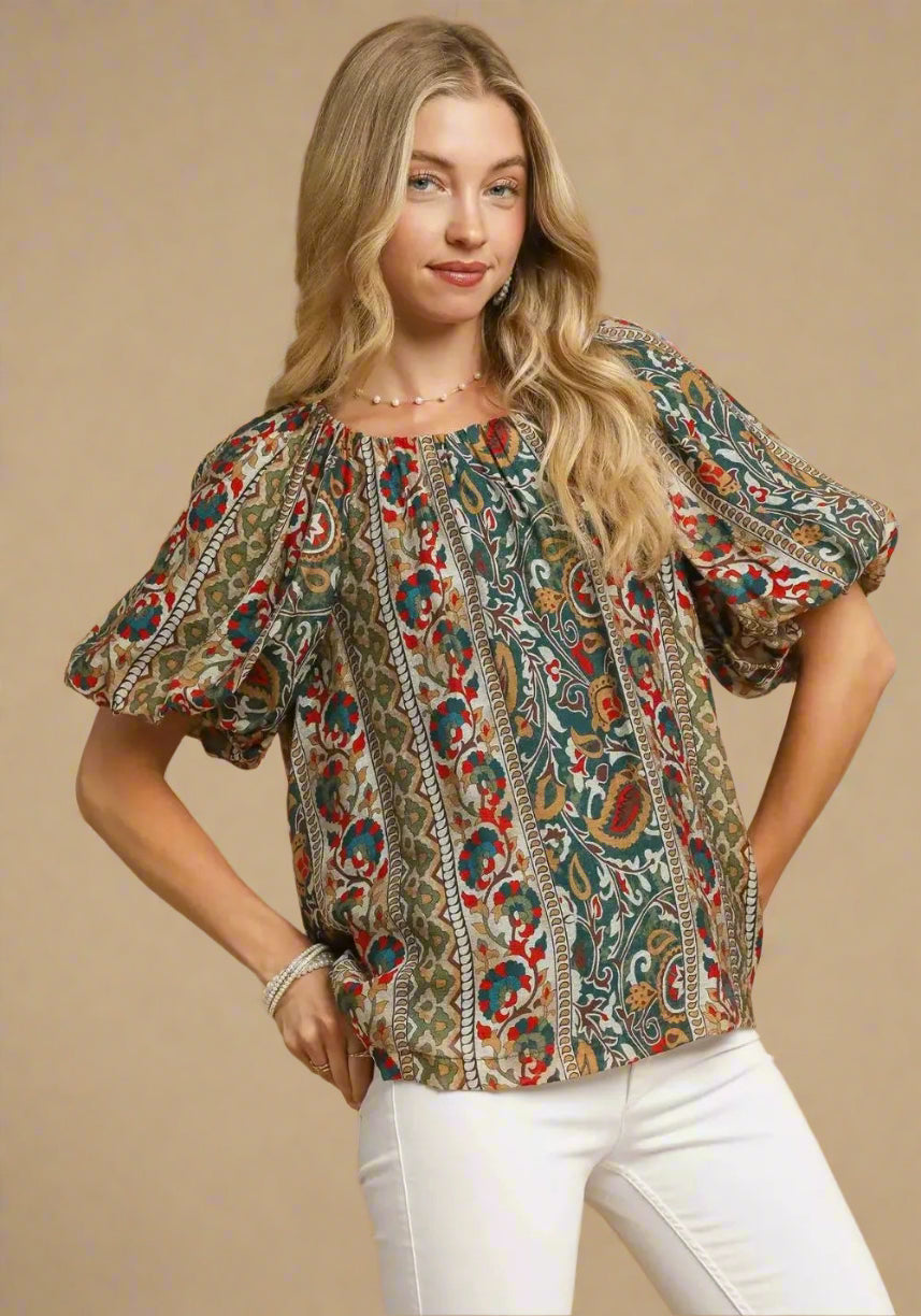 Woman wearing a patterned blouse and white pants on a beige background