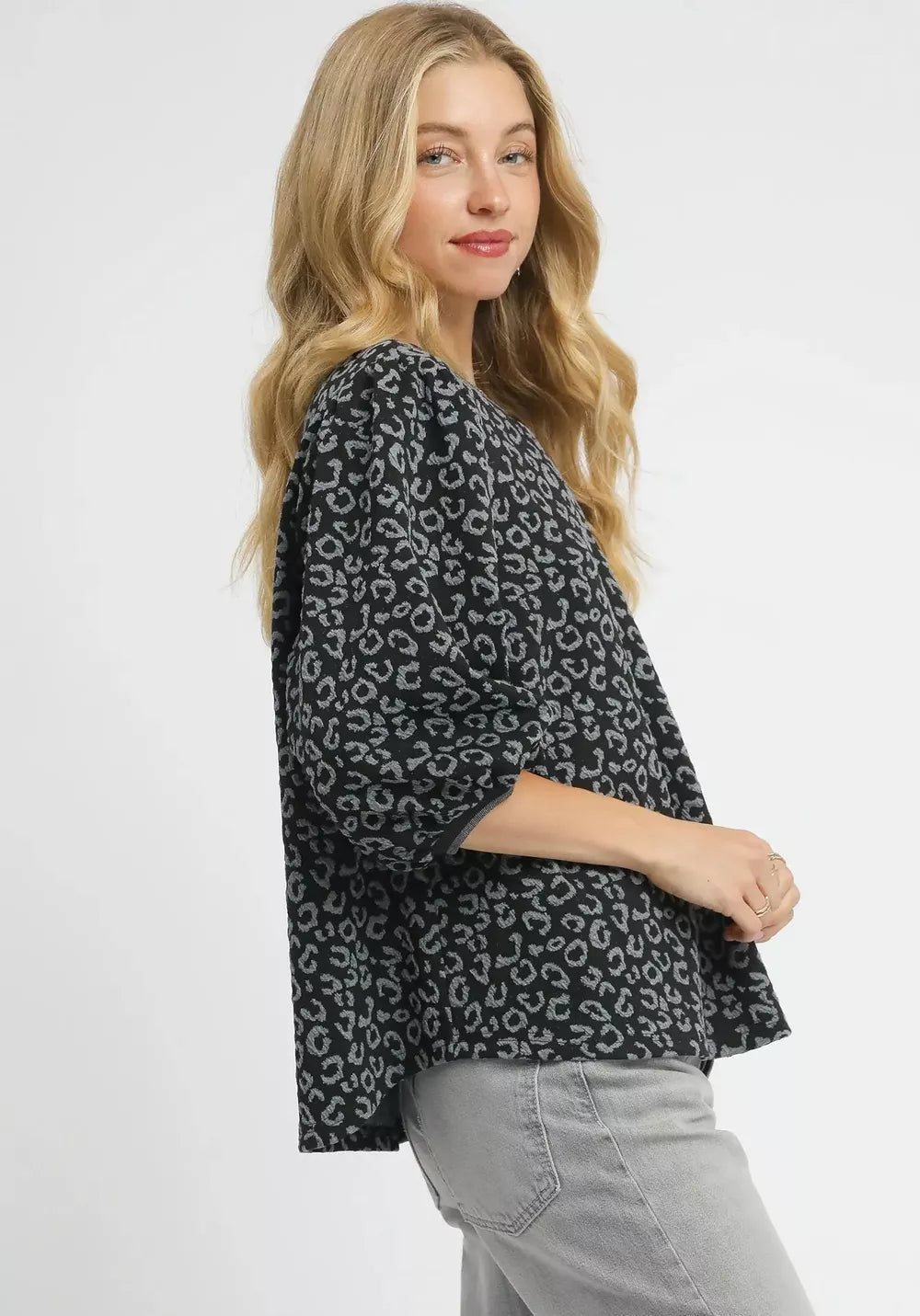 Woman wearing a black leopard print top with gray pants on a white background