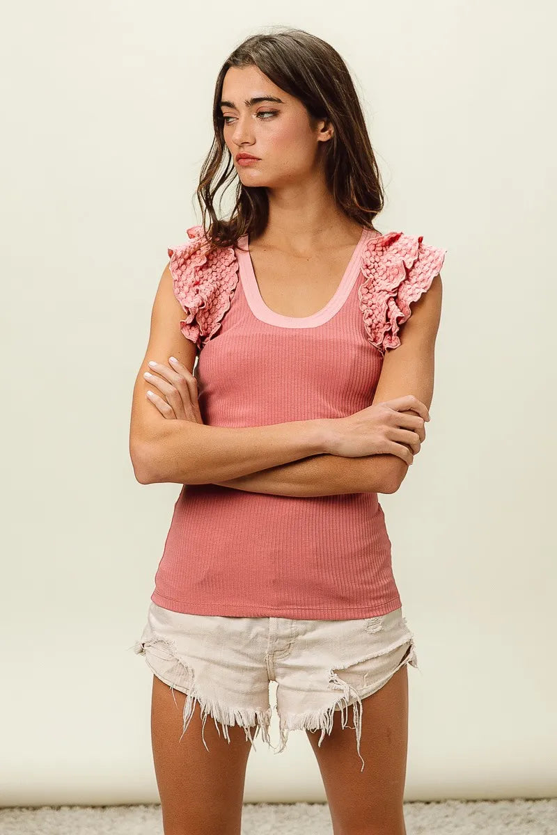 Woman wearing a pink sleeveless top with ruffled shoulders and white shorts against a plain background