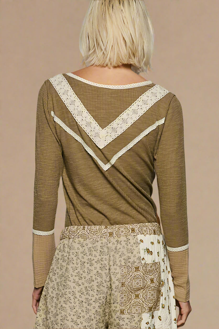 Person wearing a green long-sleeve top with lace details and patterned pants on a plain background