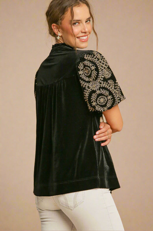 Woman wearing a black blouse with embroidered sleeves on a beige background