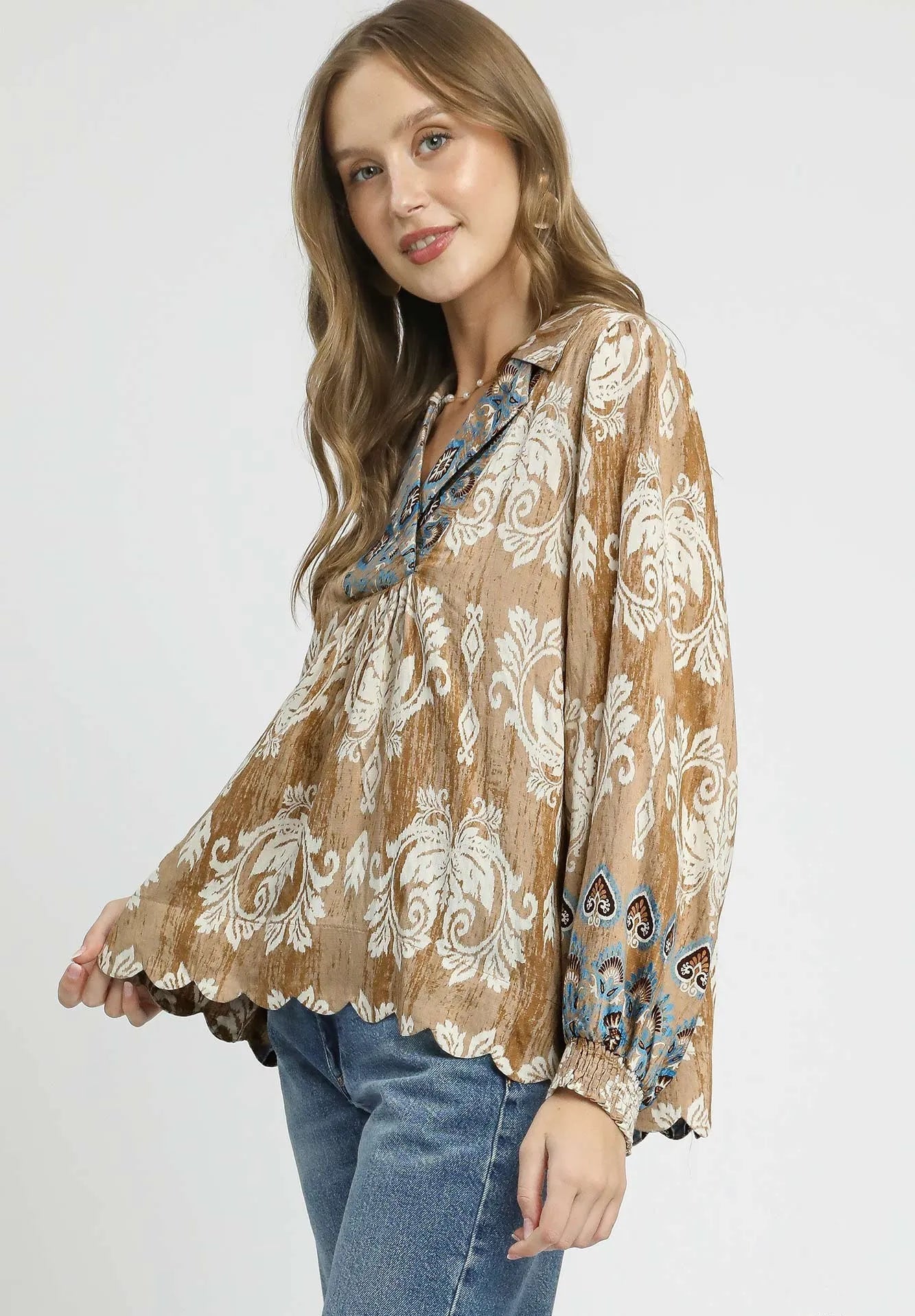 Woman wearing a beige patterned blouse with blue jeans on a white background