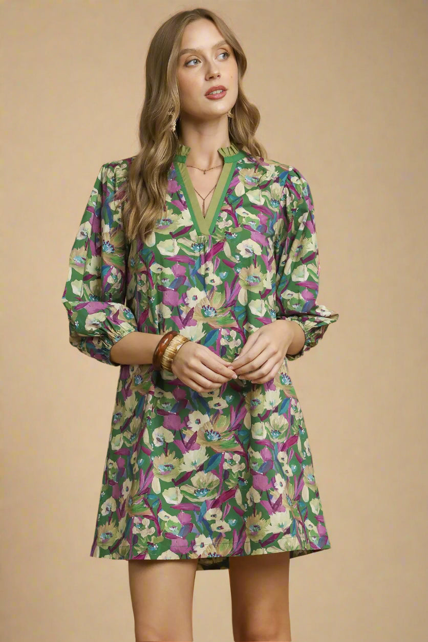 Woman wearing a floral dress with green, purple, and white pattern on a beige background