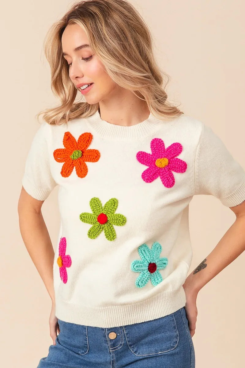 Woman wearing a white sweater with colorful flower patterns on a beige background