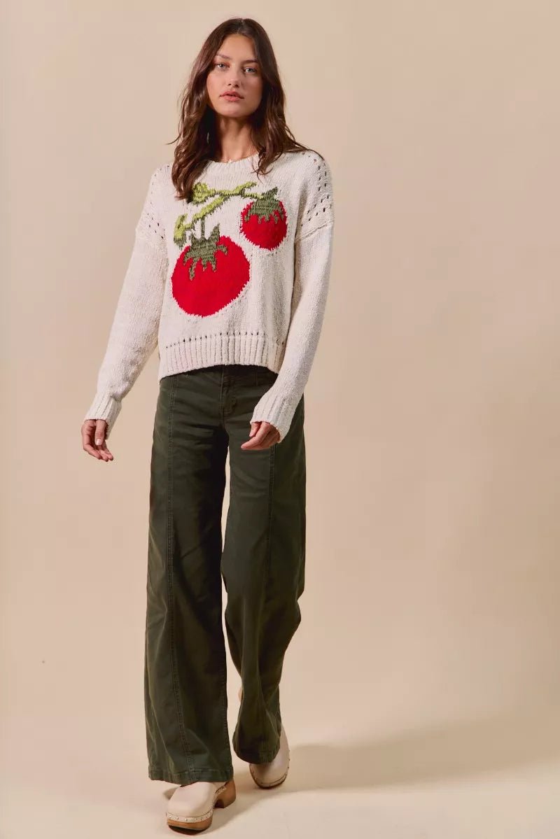 Woman wearing a white sweater with red apple design against a beige background