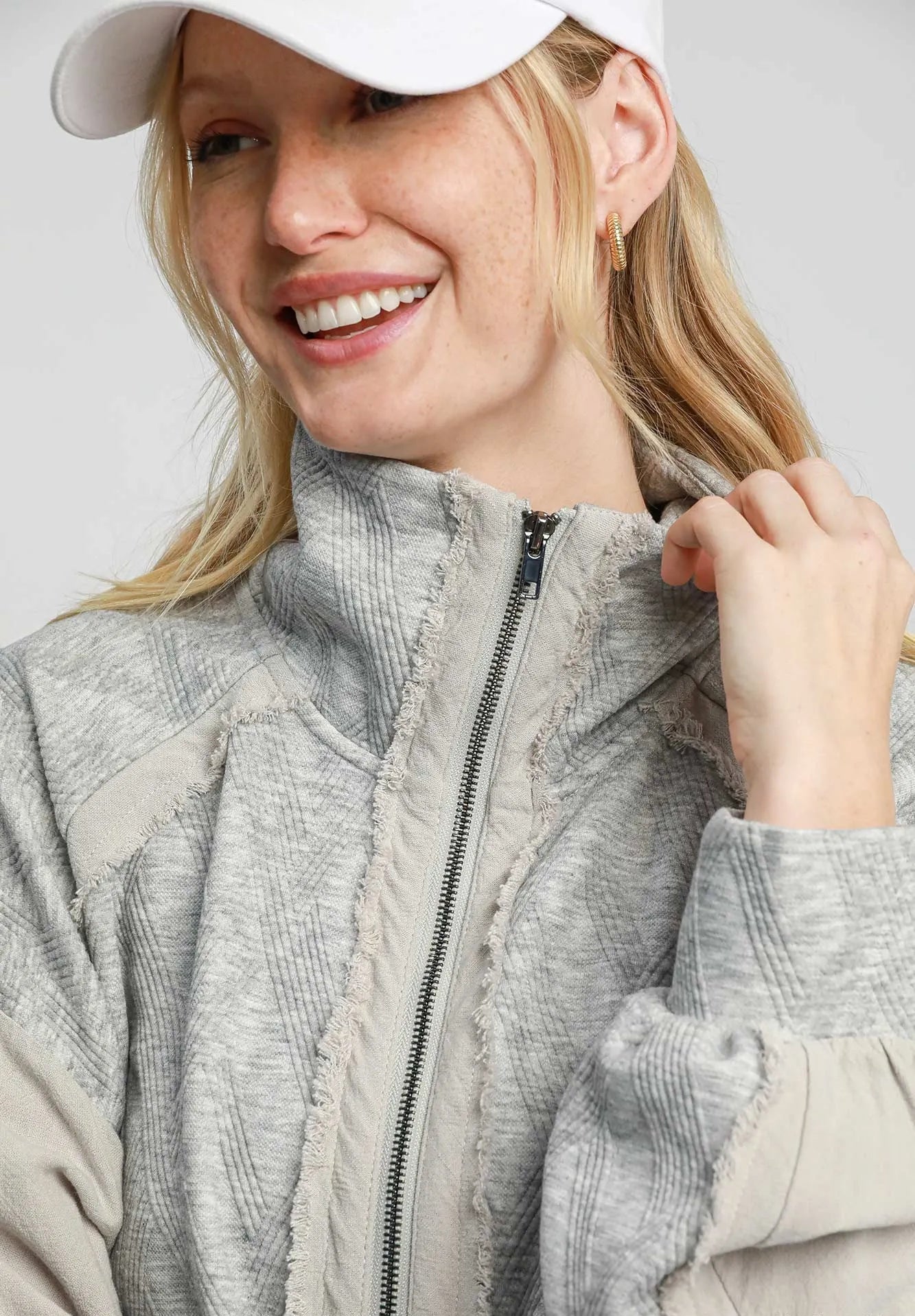 Woman wearing a gray textured jacket with a white cap on a light gray background