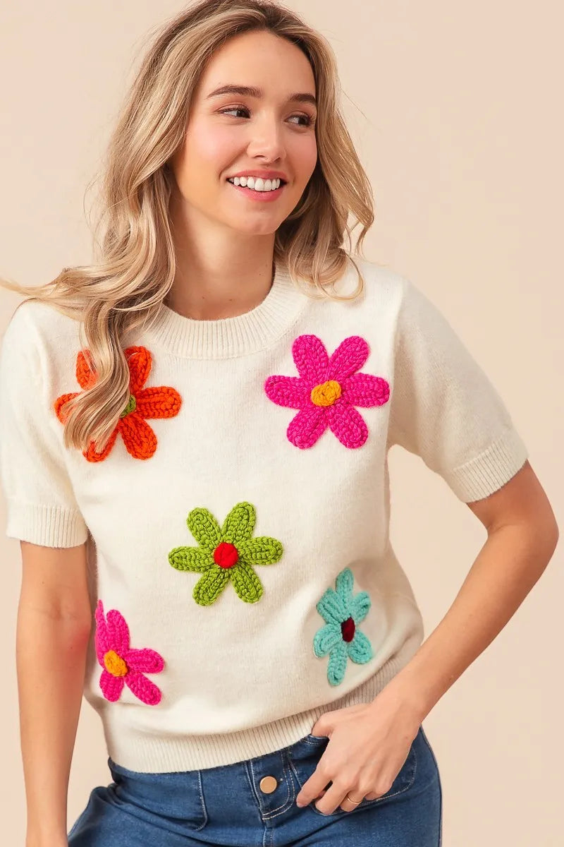Woman wearing a white sweater with colorful flower patterns on a beige background