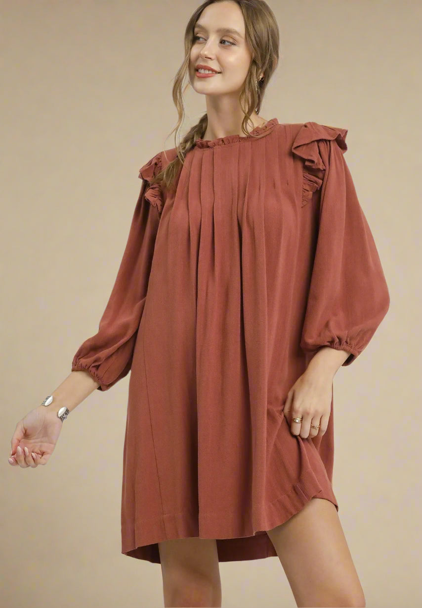 Woman wearing a rust-colored dress with ruffled sleeves on a beige background
