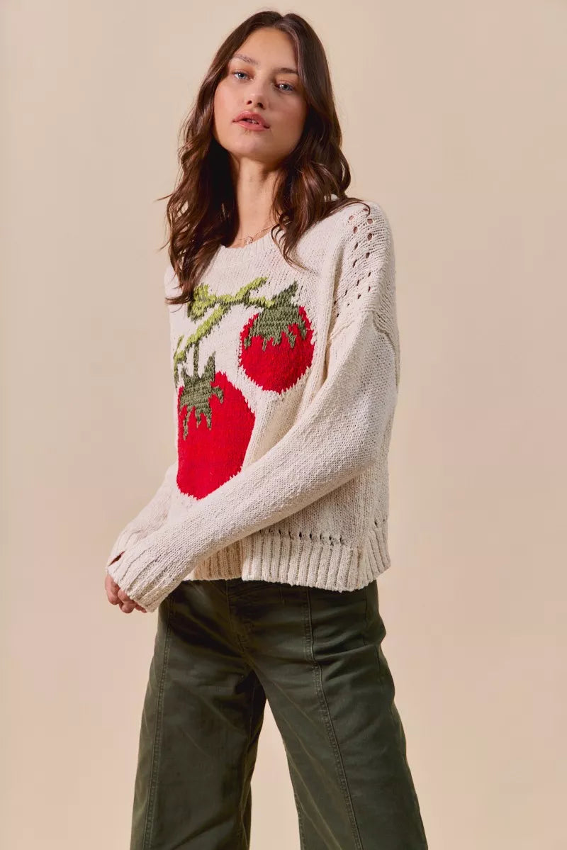 Woman wearing a cream sweater with red apple design against a beige background