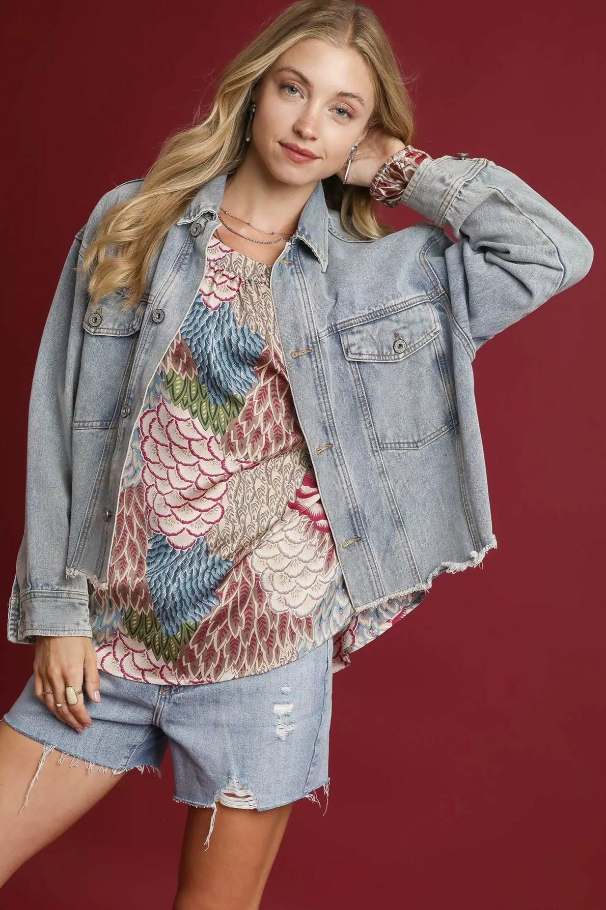 Woman wearing a denim jacket over a patterned top and shorts on a red background