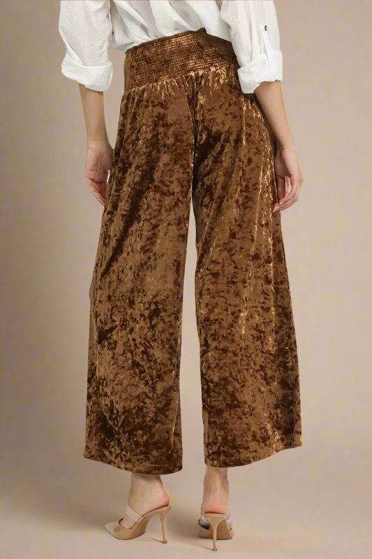 Brown crushed velvet pants worn by a person on a beige background