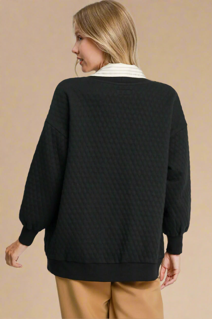 Person wearing a black textured sweater on a plain background