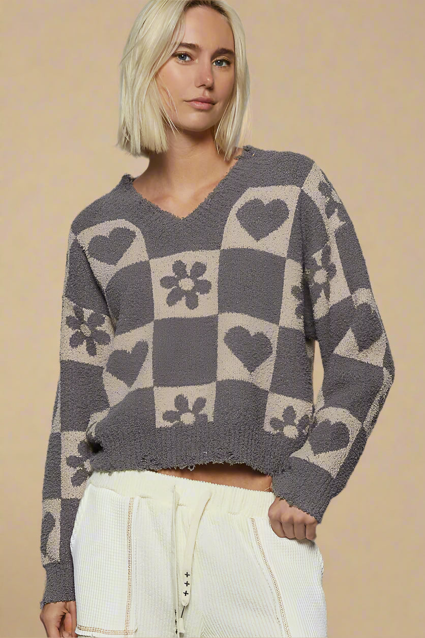 Person wearing a gray and beige checkered sweater with heart and flower pattern against a plain background