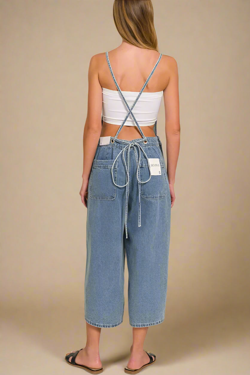 Woman wearing a white crop top and blue wide-leg overalls on a beige background