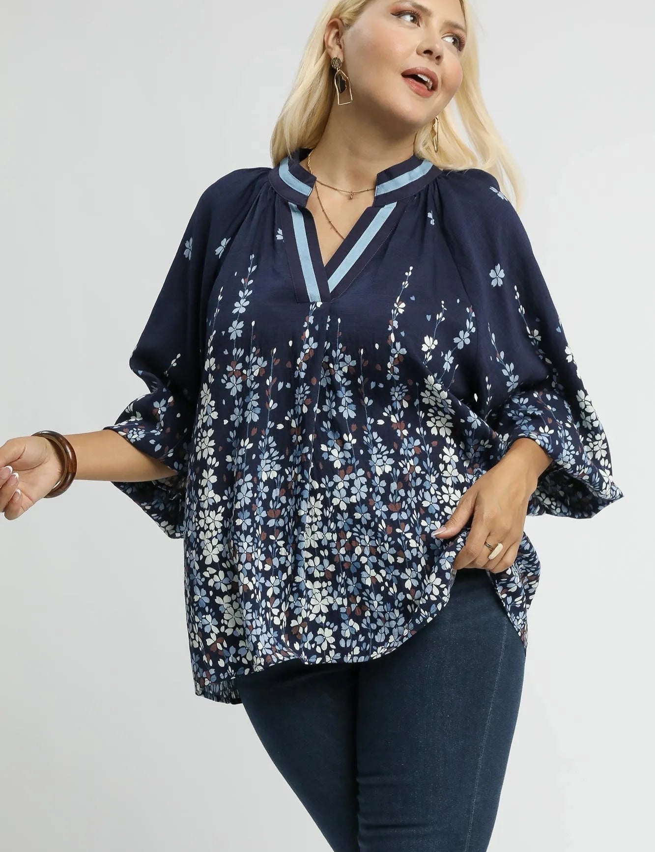 Woman wearing a navy floral blouse with bell sleeves on a white background